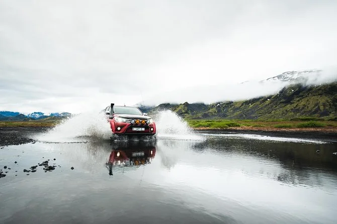 A red Arctic Trucks pickup on oversized tyres splashing through a river