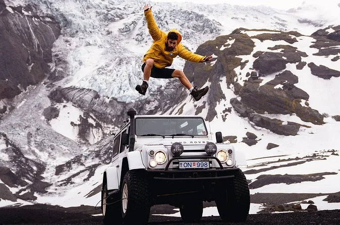 Ein Mann springt im Schnee über einen weißen Jeep