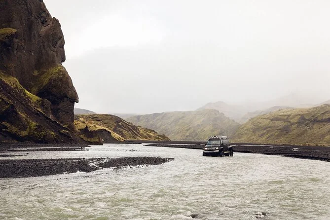 Un superjeep en una ancha llanura fluvial de grava bajo las montañas