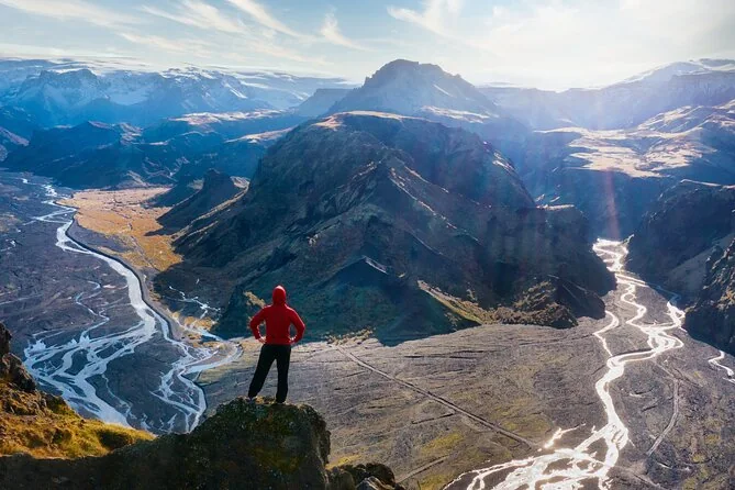 Un excursionista con chaqueta roja de pie sobre un valle glaciar de ríos trenzados