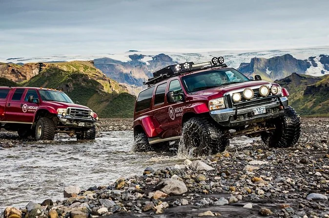 Two red Midgard super jeeps standing in a shallow glacial river