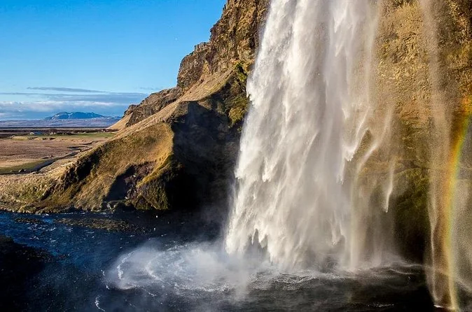 La cascada de Seljalandsfoss cayendo por un acantilado sobre un prado verde